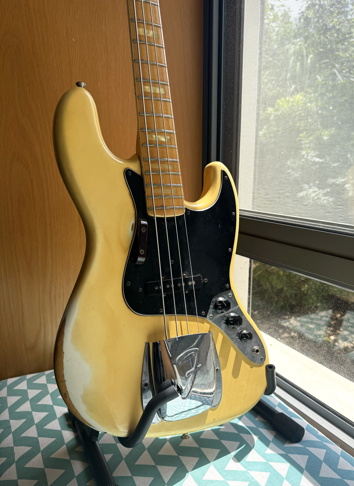 The full body of the 1975 Jazz Bass on its stand, worn blonde finish in the window light