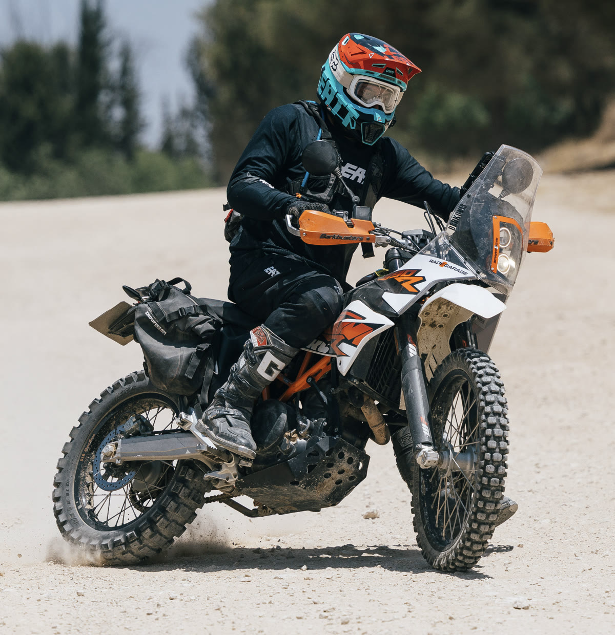 David standing on the pegs of the KTM 690 Rally, kicking up dust on a gravel road