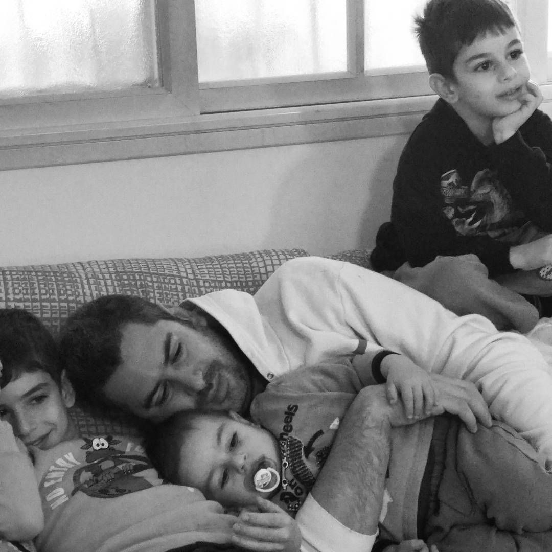 David on the couch under a pile of his three boys, the little one with a pacifier