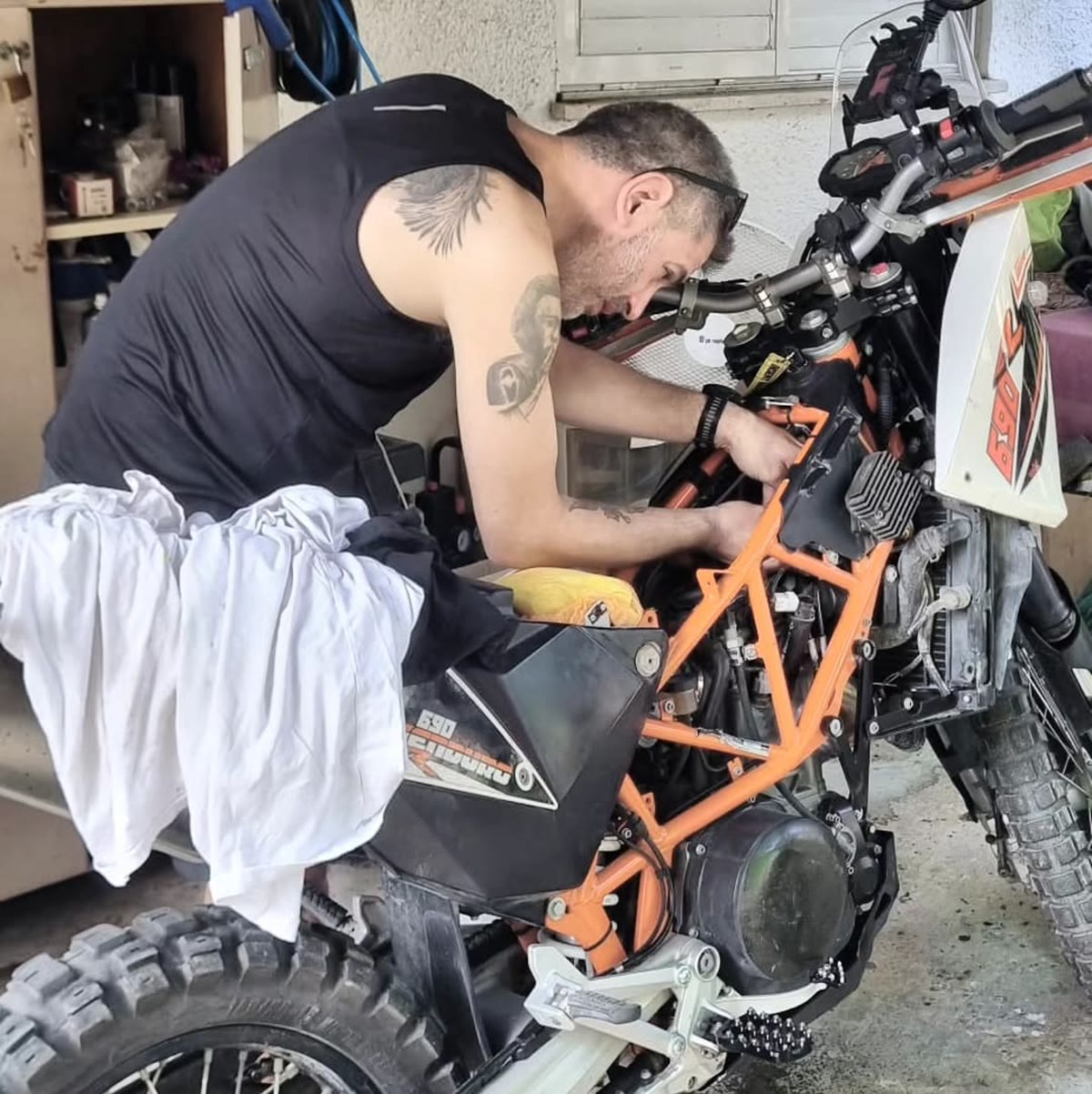 David leaning over the stripped frame of his KTM 690 in the garage, wrenching