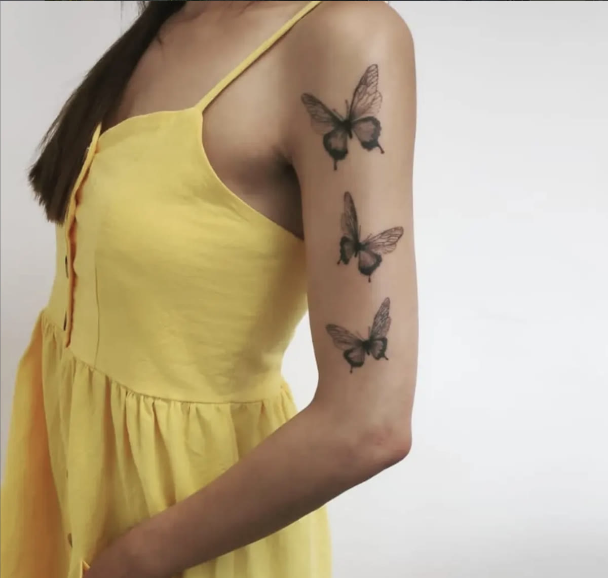 Three fine-line butterfly tattoos by David down a woman's upper arm