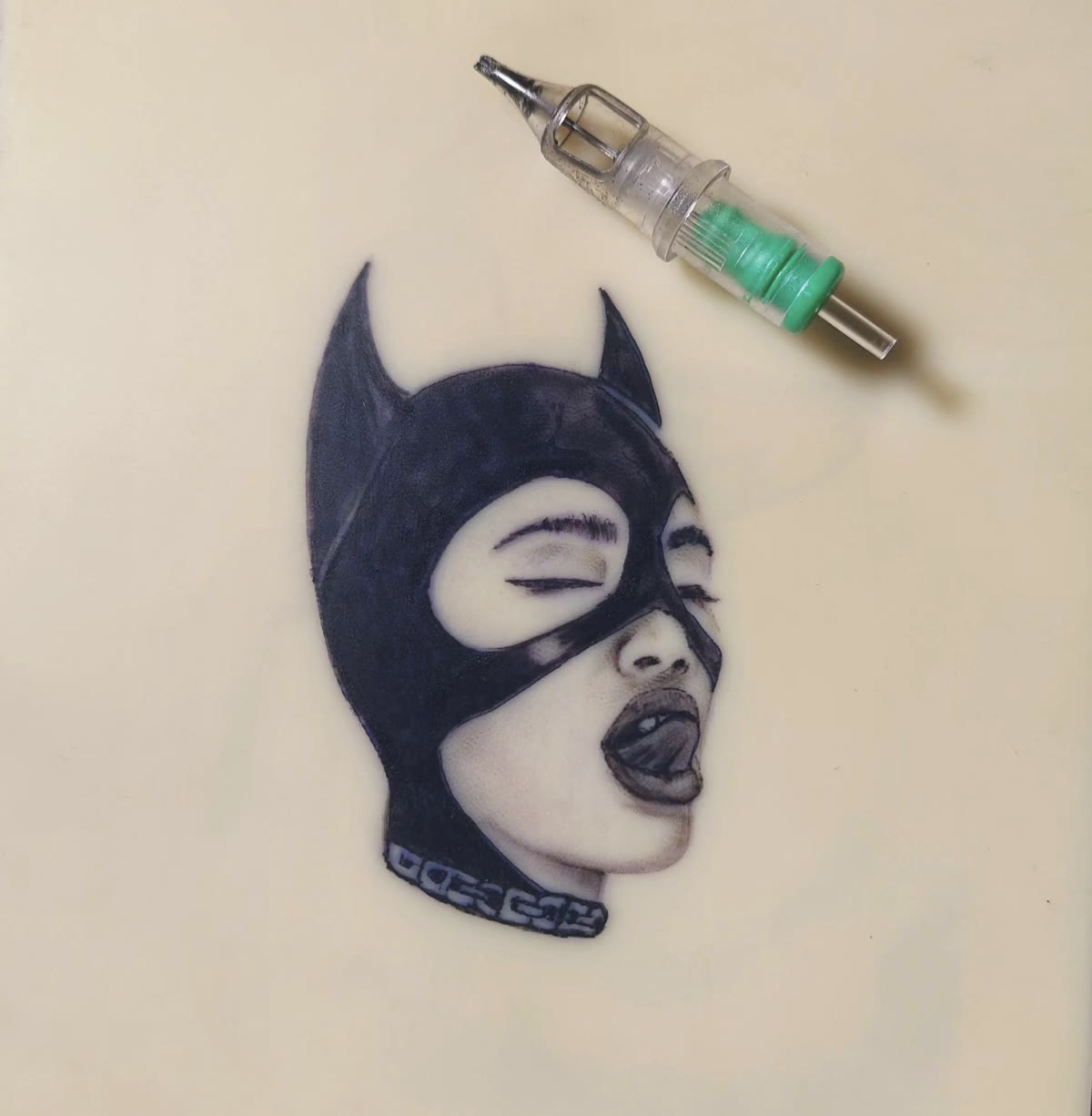 Catwoman portrait tattooed on practice skin, needle cartridge beside it