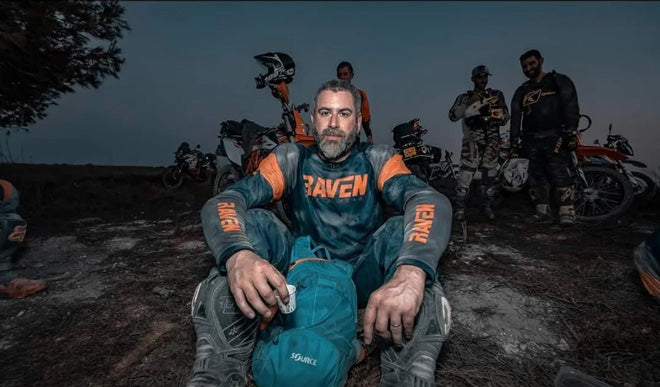 Dust-covered rider sitting on the ground at dusk, riding buddies and adventure bikes behind him